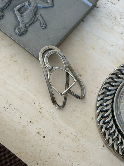 Stirrup buckle money clip on travertine beside a pewter relief box and curb chain dish, the strap finely engraved