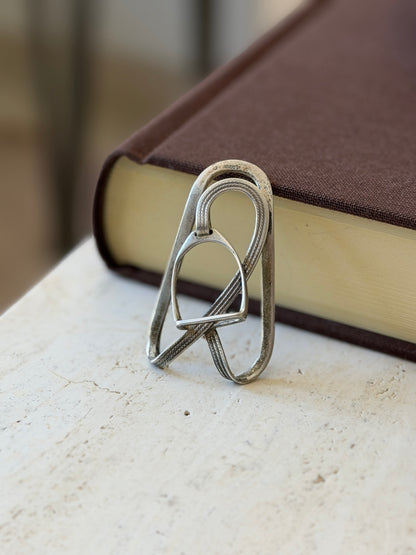 Close view of the Hermes stirrup clip propped on a book, the HERMES stamp visible at the top of the loop