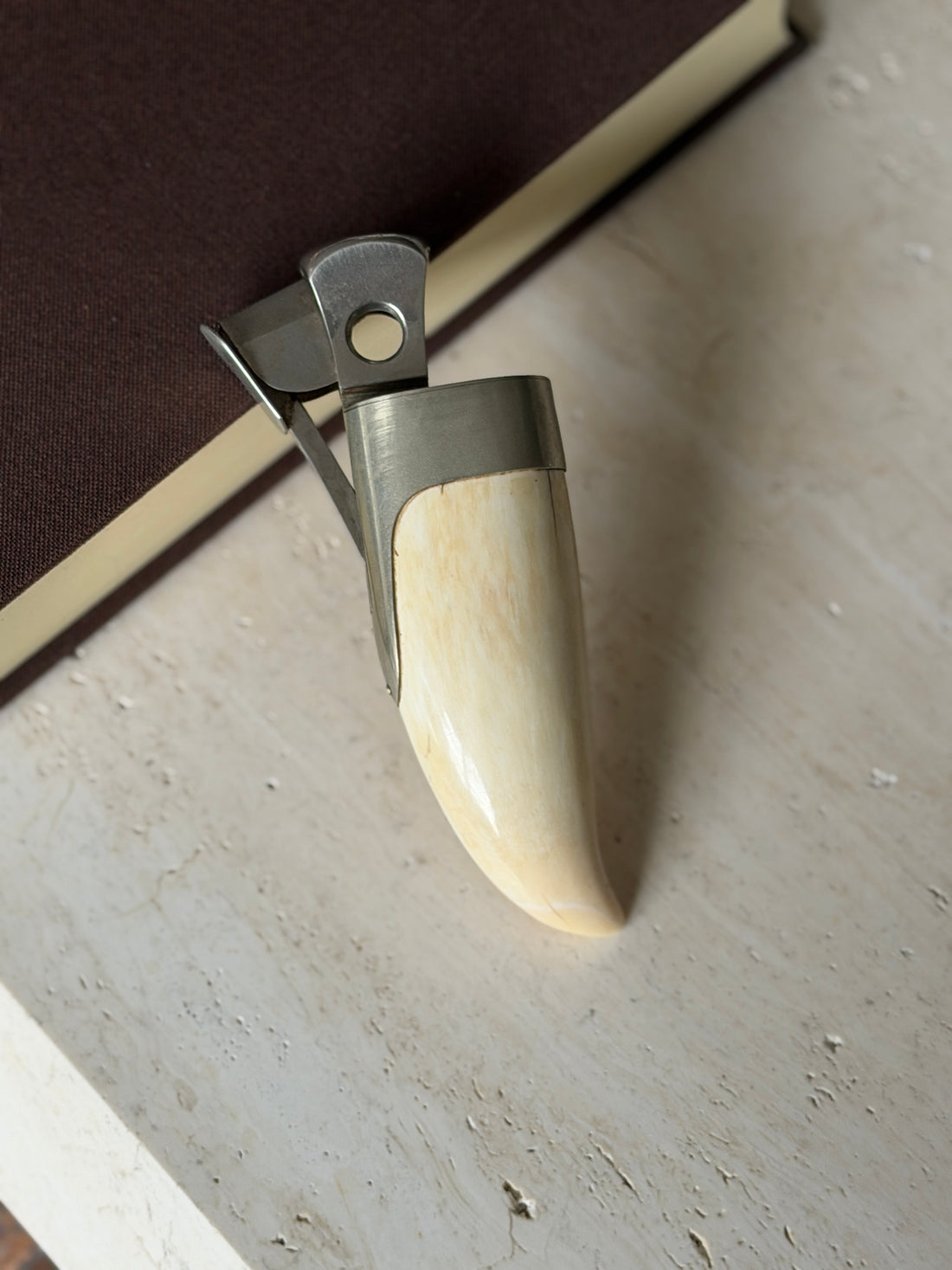 Hermes cigar cutter made from a curved whale tooth set in a brushed silver mount, with an open guillotine blade and lever, on travertine