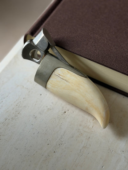 Whale tooth cigar cutter propped against a book spine, the cutting ring and spring lever opened above the silver mount