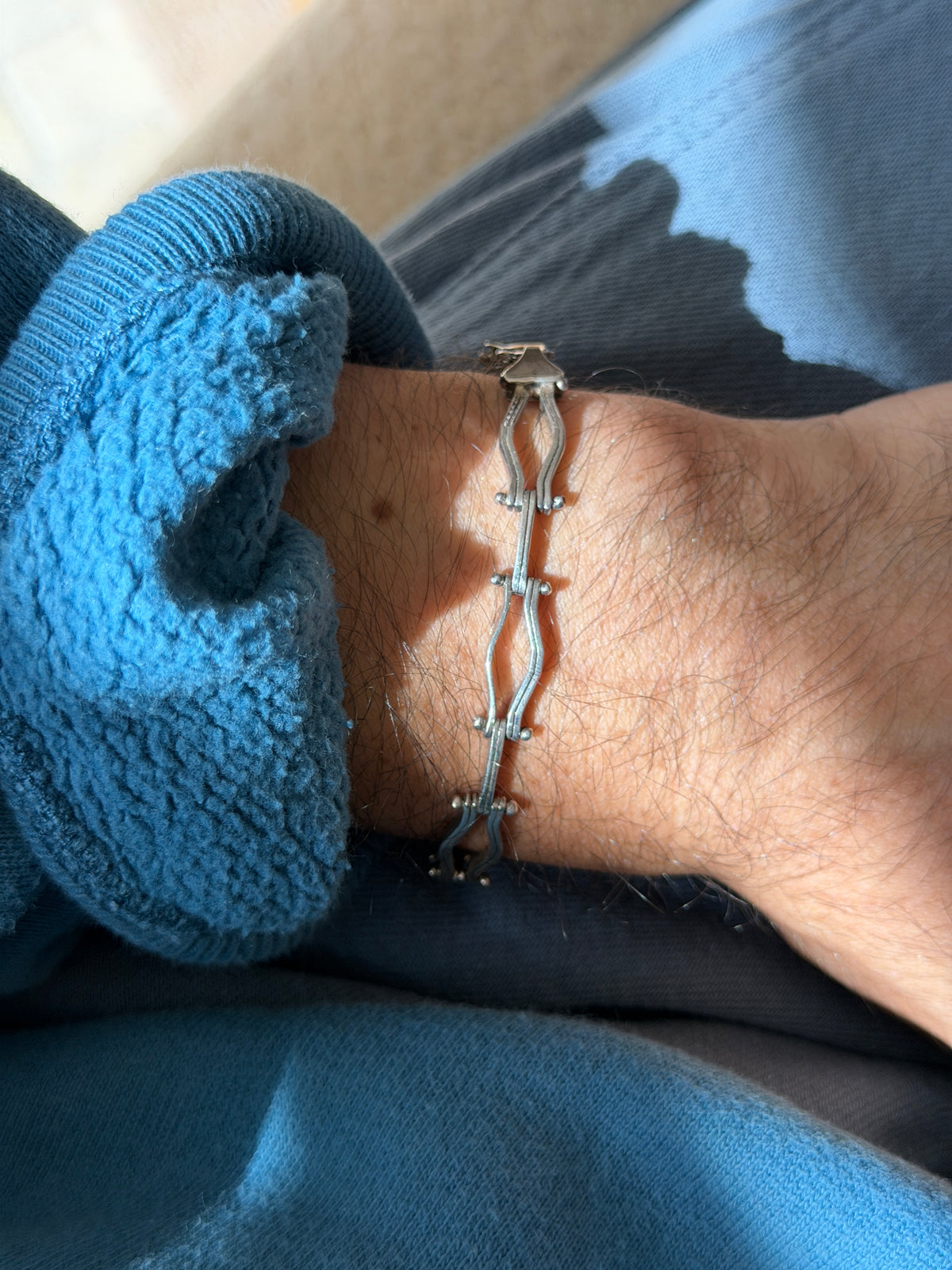 Sterling silver bracelet of hinged double wave links joined by pinned gates, worn on the wrist in bright sun with the clasp visible