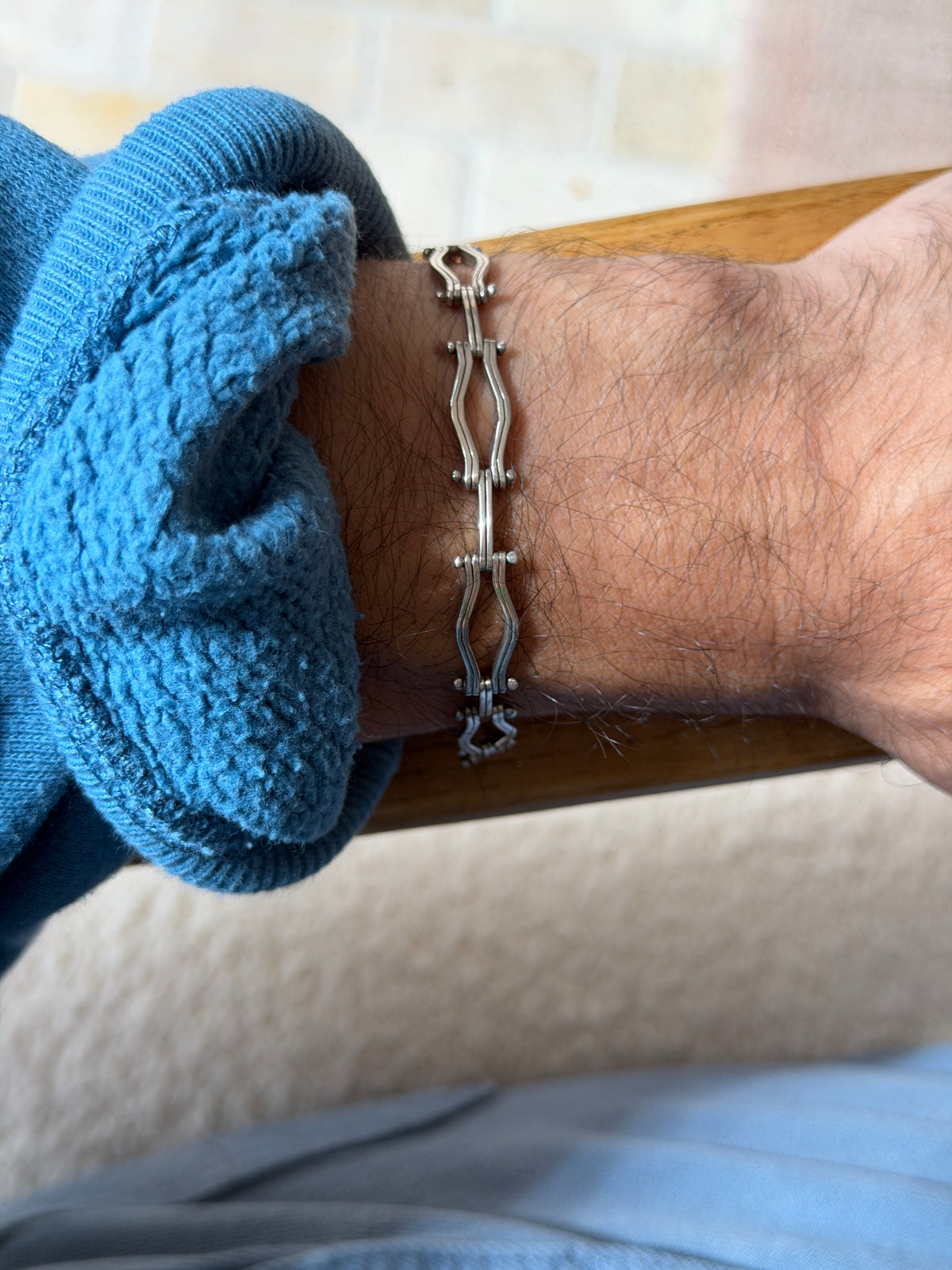 Gated link bracelet worn on a wrist resting on a wooden chair arm, showing the undulating double rails of each link