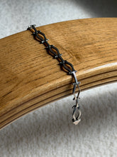 Sterling silver hinged link bracelet draped over a bentwood oak chair arm, the oxidized recesses and box clasp end visible