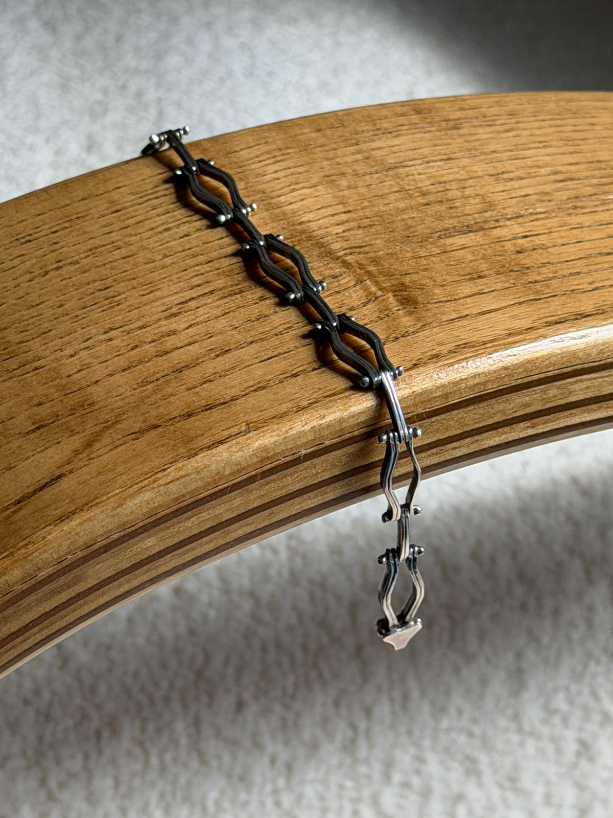 Sterling silver hinged link bracelet draped over a bentwood oak chair arm, the oxidized recesses and box clasp end visible