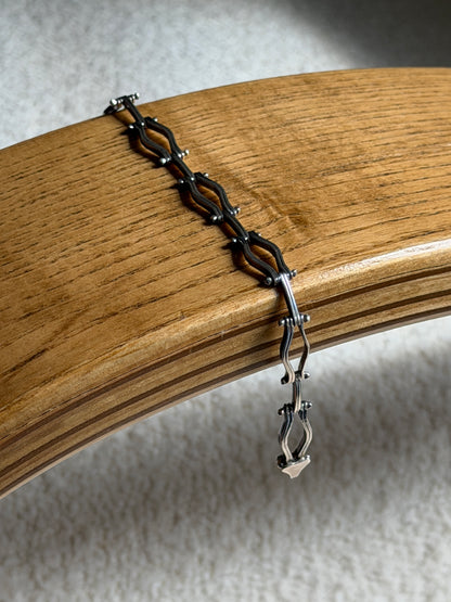 Sterling silver hinged link bracelet draped over a bentwood oak chair arm, the oxidized recesses and box clasp end visible