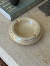 Top-down view of round cream glazed ceramic vide poche with gold detailing styled on travertine surface from Collectors Gene