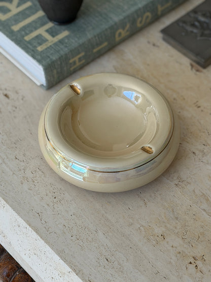 Top-down view of round cream glazed ceramic vide poche with gold detailing styled on travertine surface from Collectors Gene
