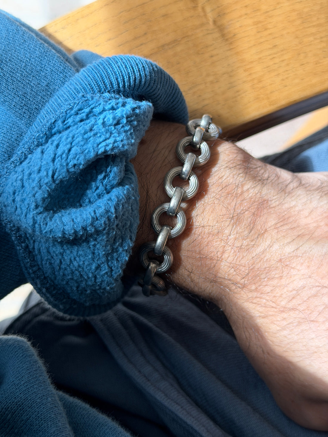 Textured ribbed link bracelet on the wrist against a wooden chair arm, the concentric grooves of each ring in raking light