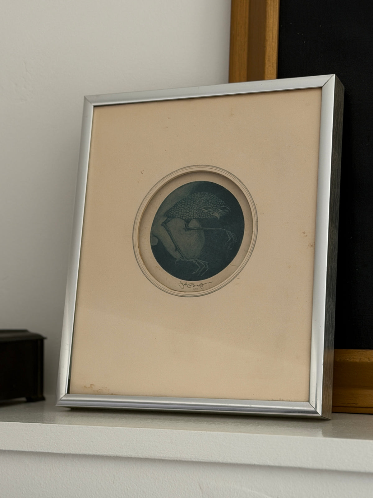 Framed Nightbird mezzotint leaning on a white shelf beside a small dark box and a gilt framed painting