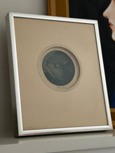 Angled view of the framed John P. Morgan print on a shelf, the silver frame edge catching light against a dark portrait behind