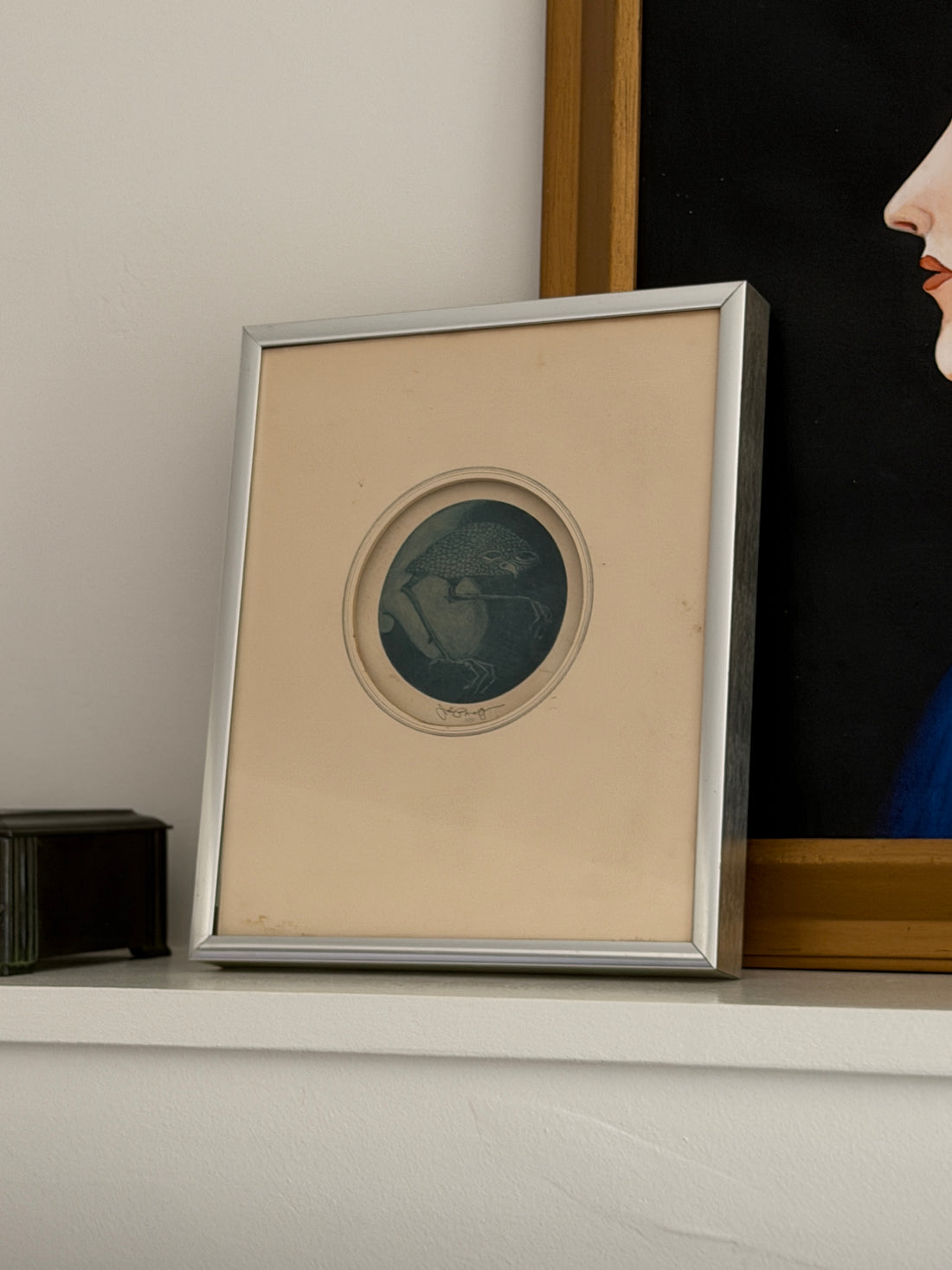 Nightbird mezzotint in its silver frame on a white mantel shelf, styled between a bronze box and a large portrait painting