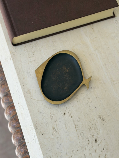 Karl Hagenauer fish ashtray in brass with a blackened oval bowl, resting on a travertine table beside a brown clothbound book
