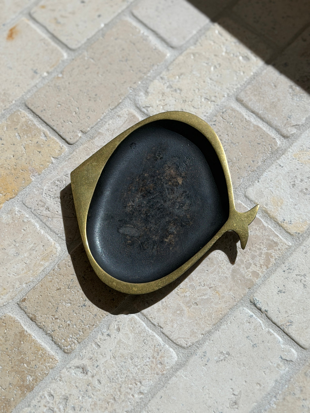Hagenauer fish ashtray from Vienna on a tumbled stone floor in raking sunlight, highlighting the worn patina inside the blackened bowl