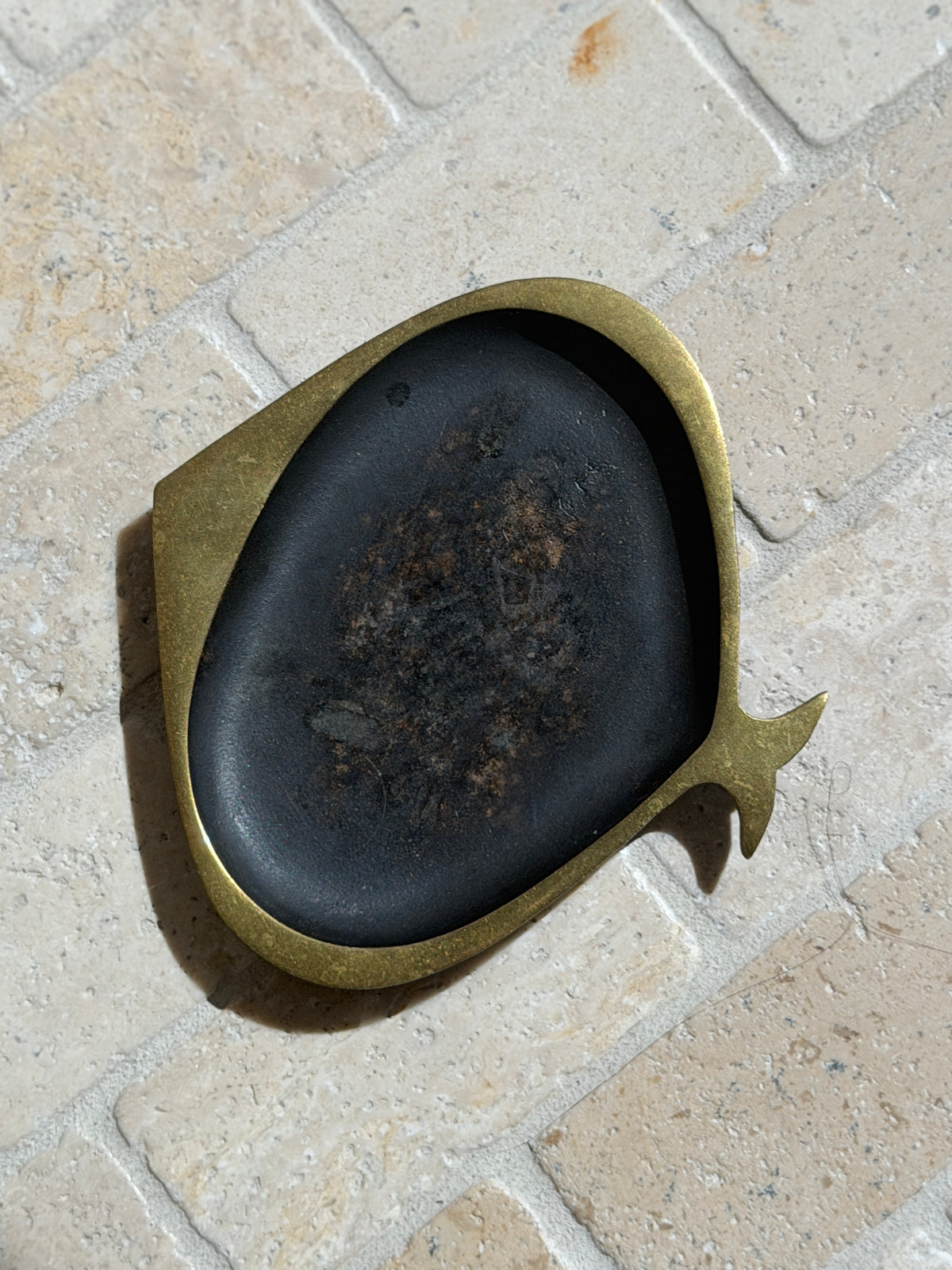 Close top view of the Austrian brass fish ashtray, detailing the brushed brass outline, angular head, and mottled patina across the bowl