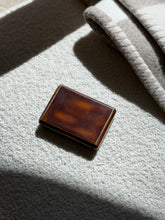 Keller Paris lacquer box on a cream boucle surface in raking sunlight, light surface wear visible on the polished lid