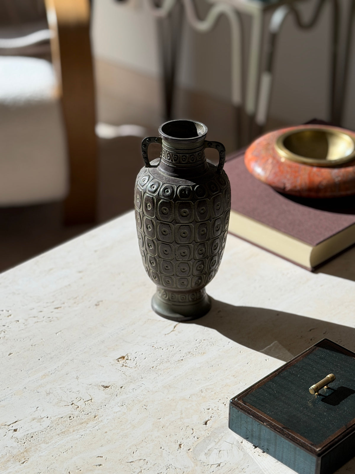 Japanese bronze baluster vase with two studded loop handles, its body cast in rows of raised rounded squares with ring and dot centers, on travertine in sunlight