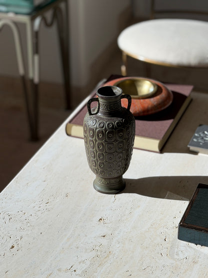 Meiji bronze vase on a travertine table beside a brown book and red stone ashtray, a long shadow cast by the raking light