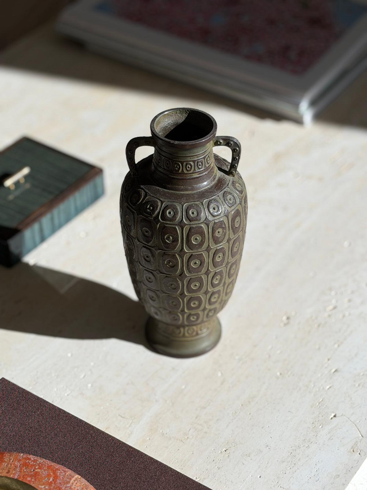 High angle view into the mouth of the bronze vase, showing the mottled interior, banded neck, and dotted handles