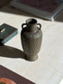 High angle view into the mouth of the bronze vase, showing the mottled interior, banded neck, and dotted handles