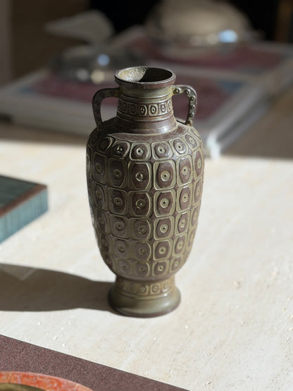 Close view of the geometric relief on the bronze vase, the green and russet patina highlighting each raised square and ring