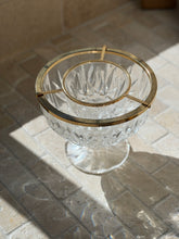 Overhead view of the cut crystal footed caviar dish with a gilt ring frame holding a smaller inner crystal bowl, on tumbled stone pavers