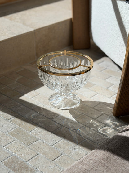 Crystal caviar service dish on stone pavers beside an oak chair leg, sunlight throwing rainbow refractions across the floor