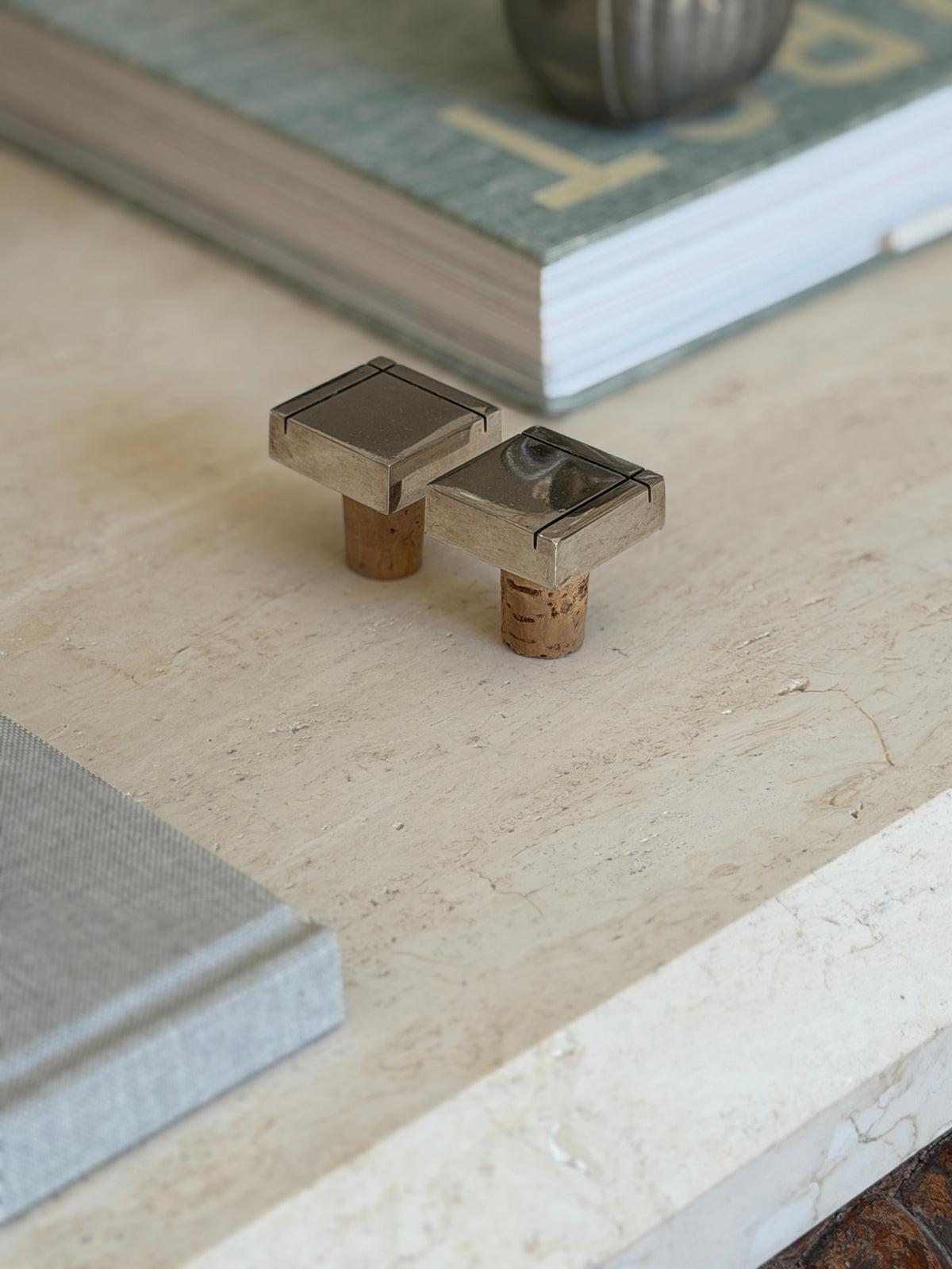 Collectors Gene pair of vintage modernist metal bottle stoppers with cork bases displayed on a travertine desk