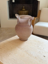 Front view of the Murano scavo glass amphora vase on a travertine table, with a brick fireplace and lidded brass pot visible behind it