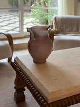Angled view of the amphora vase on a coffee table with a barley-twist wood base, framed by garden doors and a monogrammed pillow in the background