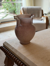 Full view of the vase at a slight angle showing its handled silhouette, with a teal ceramic vase and dried branches visible behind it