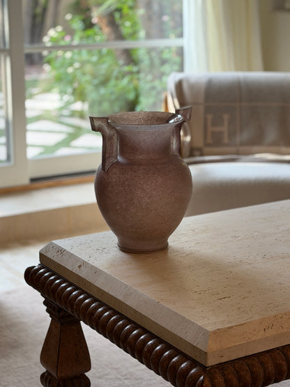 Front view of the vase on the travertine table with a cream sofa and garden view in the background