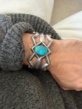 Dine sand cast silver cuff with an oval spiderweb turquoise cabochon at the center of angular open bars, worn on the wrist against a gray knit sleeve