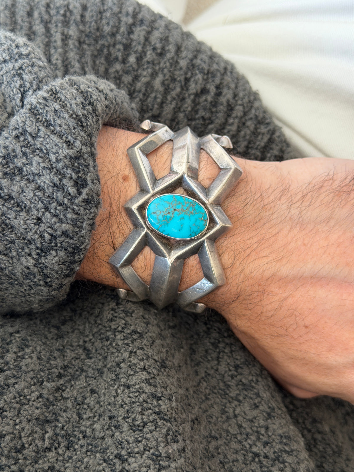 Sand cast silver cuff on the wrist, the faceted bars radiating from the bezel set turquoise toward pointed and curled terminals