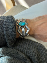 Wrist view of the Dine cuff against cream trousers, the scrolled end terminals visible beneath the turquoise center