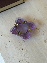 Lavender neodymium glass ashtray with a four lobed rim and a brass ring insert fitted with four cigarette rests, on a travertine tabletop