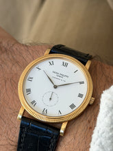 The watch worn on the wrist from another angle, dial turned toward the camera, against a tan fabric background