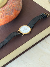 Watch displayed on a brown book next to an orange stone bowl, the black strap fanned out in a gentle curve