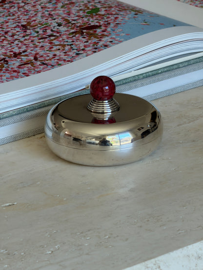 Front view of the Puiforcat candy dish on travertine, its mirror polished lid reflecting the room below the red finial