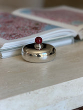Puiforcat round silver plate candy dish with a domed lid and a mottled red stone ball finial on a ribbed silver collar, beside an open art book