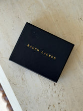 Closed black Ralph Lauren presentation box with the name stamped in gold capitals, resting on a travertine table