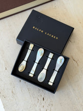 Four mother of pearl caviar spoons secured with black elastic in an open Ralph Lauren box, the gold stamped lid set behind on travertine