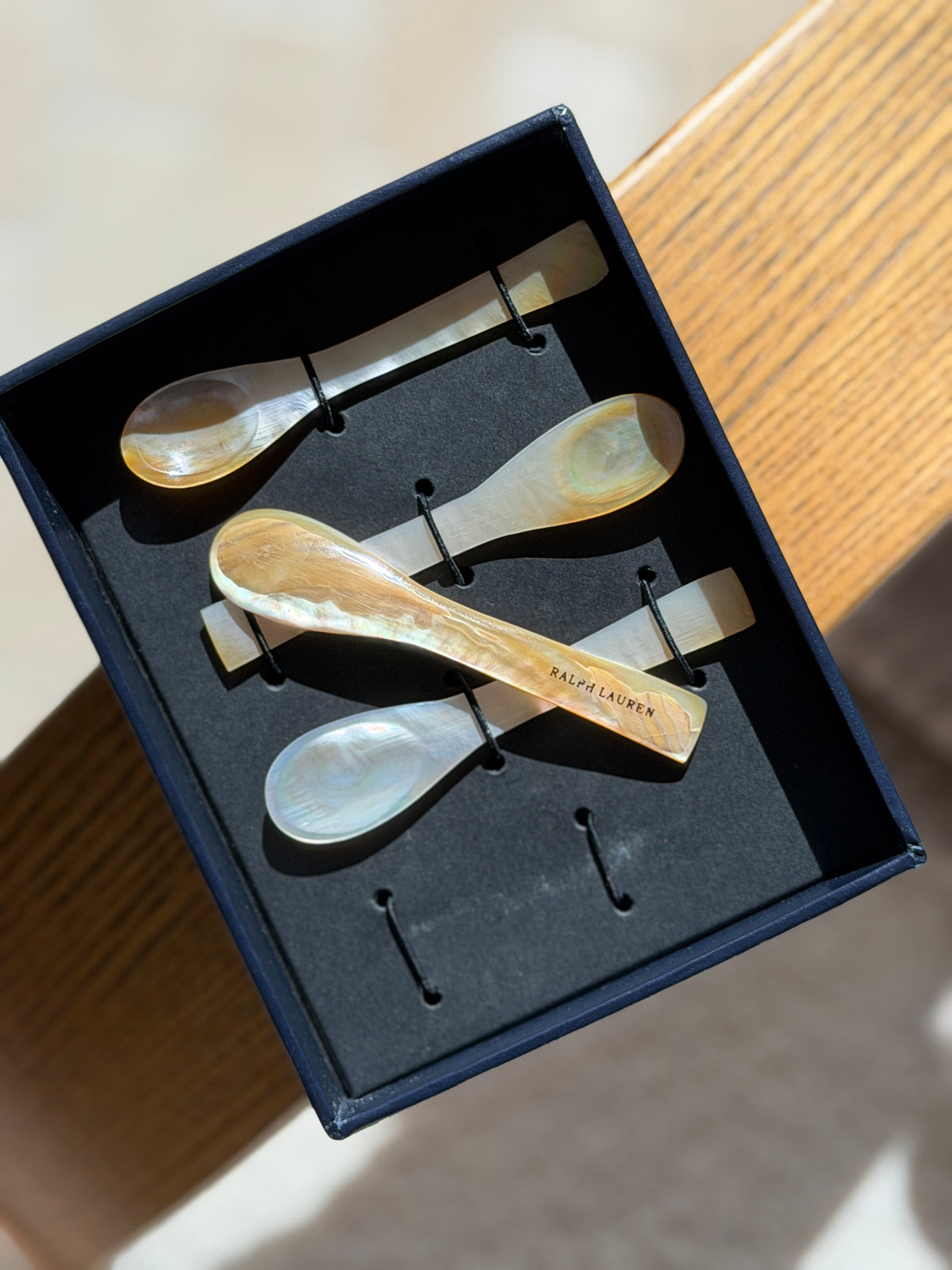 One mother of pearl caviar spoon lifted from its box, the handle engraved RALPH LAUREN across the golden shell