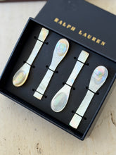 Close view of the four nacre caviar spoons in the black box, showing the rainbow sheen of each bowl and flat paddle handle