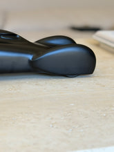 Low side view of the race car rear fairing resting on travertine, the satin black finish catching a highlight