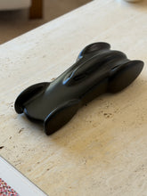 Matte black Ralph Lauren race car sculpture angled across a travertine table, the long hood leading to the cockpit slot