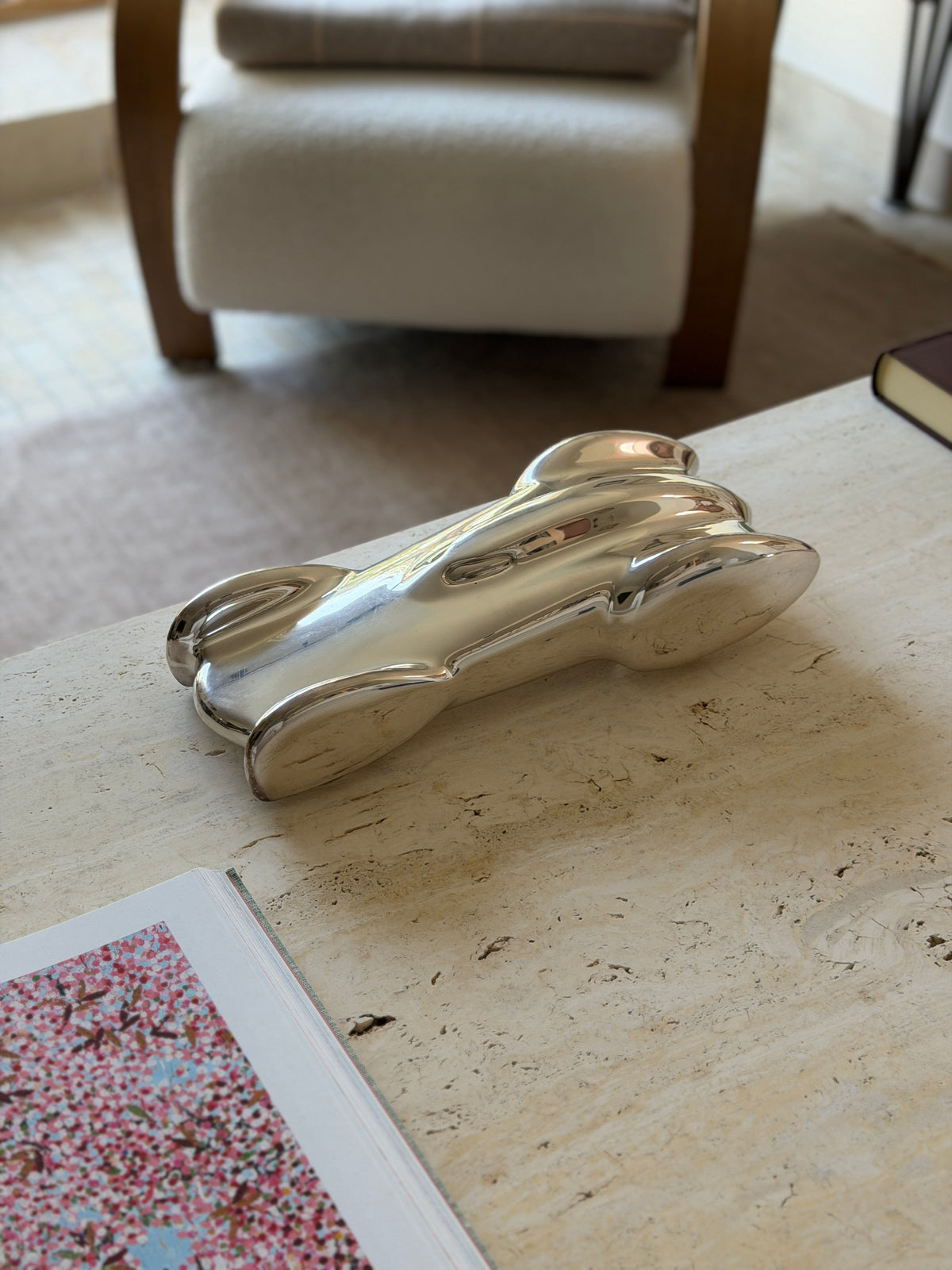 Ralph Lauren Clermont race car sculpture in polished silver tone metal on a travertine coffee table, a boucle armchair and open art book around it