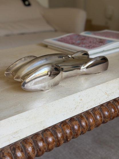 Race car sculpture at the edge of a travertine table with a bobbin turned wood apron, the bullet shaped fenders catching the light