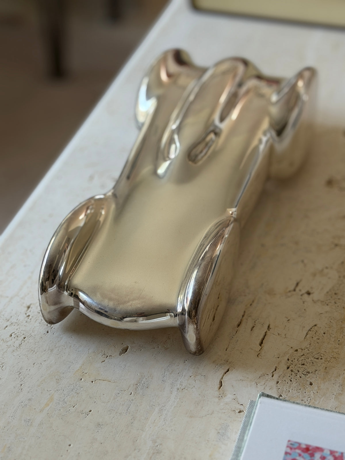 Top down view of the polished race car body on travertine, the flared rear fenders and sculpted engine cover in sharp reflection