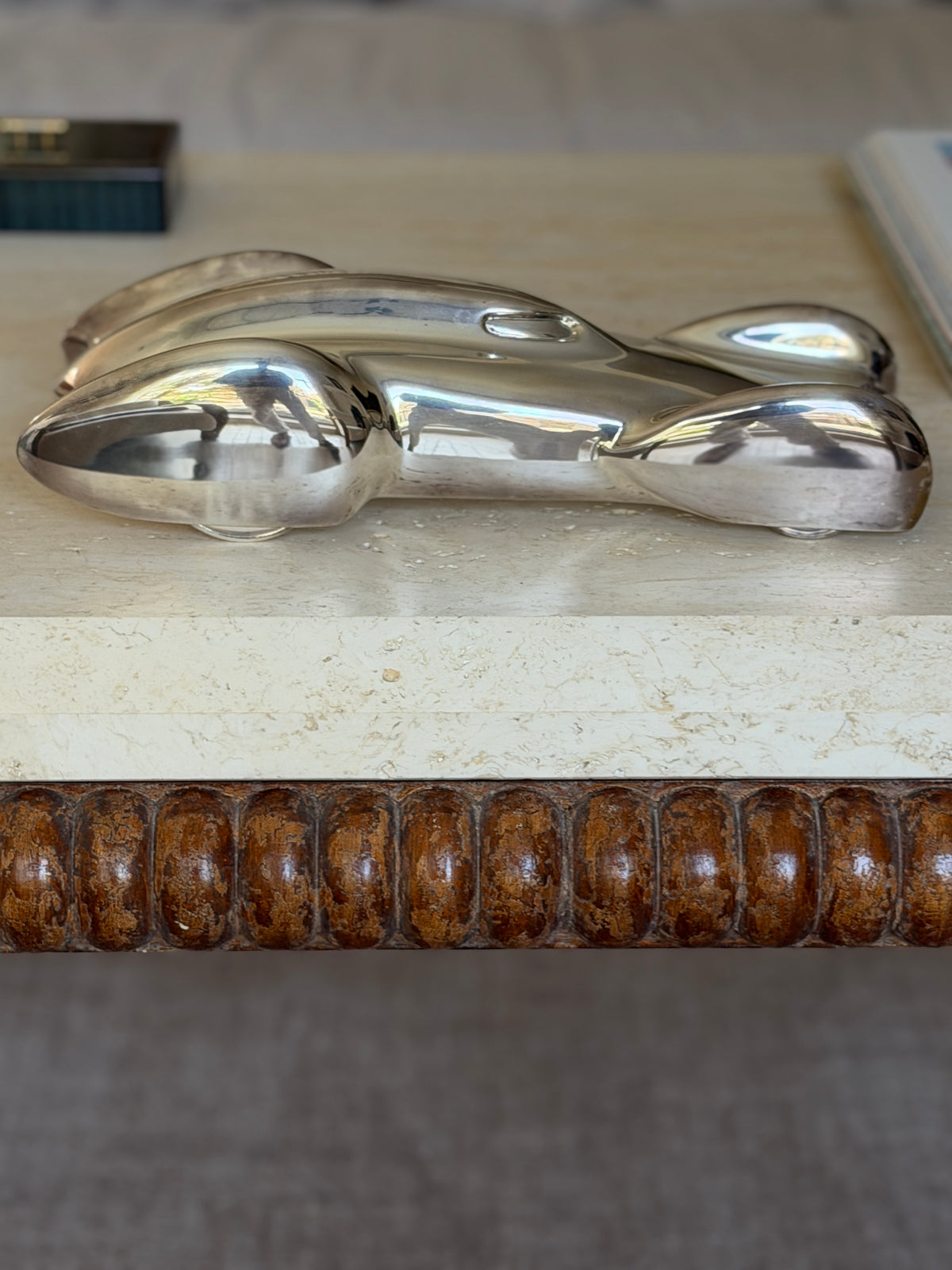 Eye level side profile of the Ralph Lauren race car sculpture on travertine, small wheels beneath the long teardrop body and bobbin turned wood below