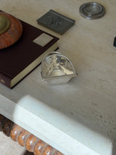 Ralph Lauren stirrup nut bowl on the corner of a travertine table among a brown book, pewter box, and chain rimmed coaster
